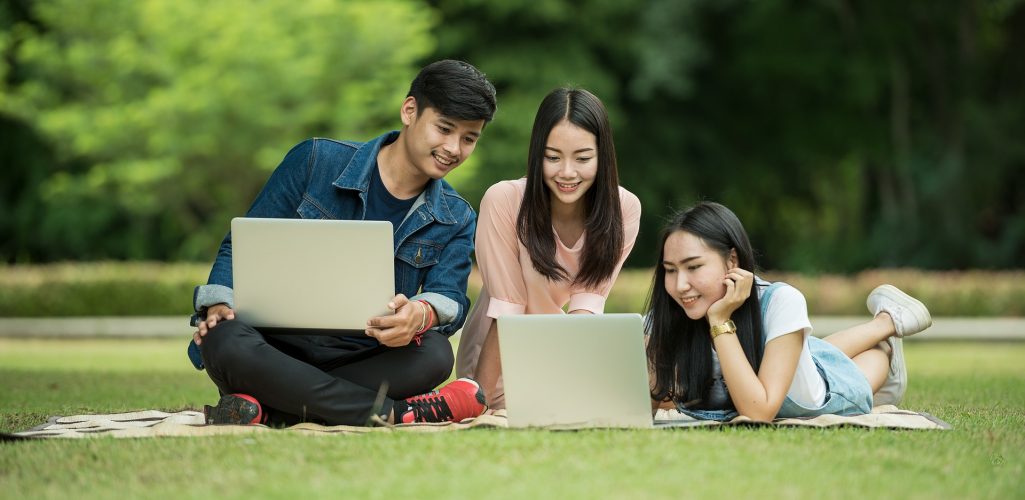 Photo of young people in a park using laptop computers